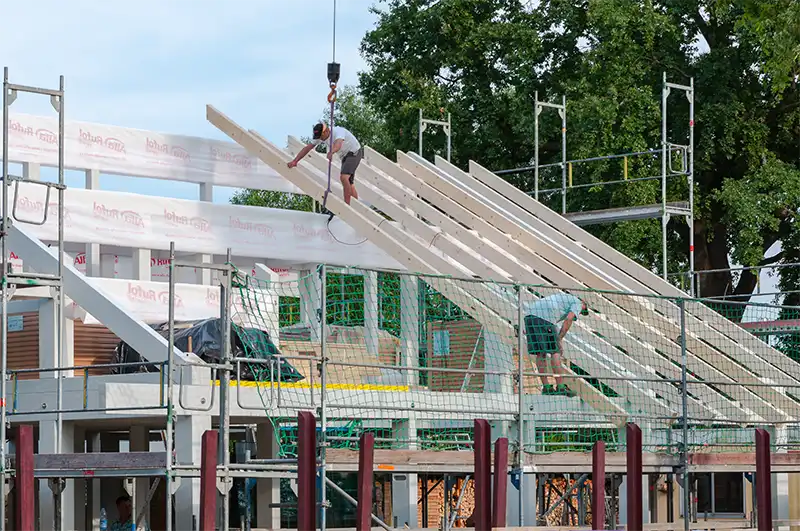 Hintergrund-Bild: Bild von Handwerkern beim Aufbau einer Dachkonstruktion eines modernen Fachwerkhauses