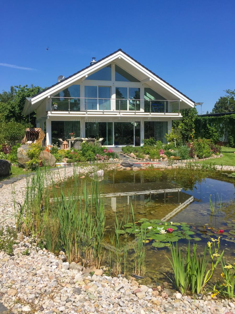 Ein modernes Fachwerkhaus vor Teichanlage im Grünen